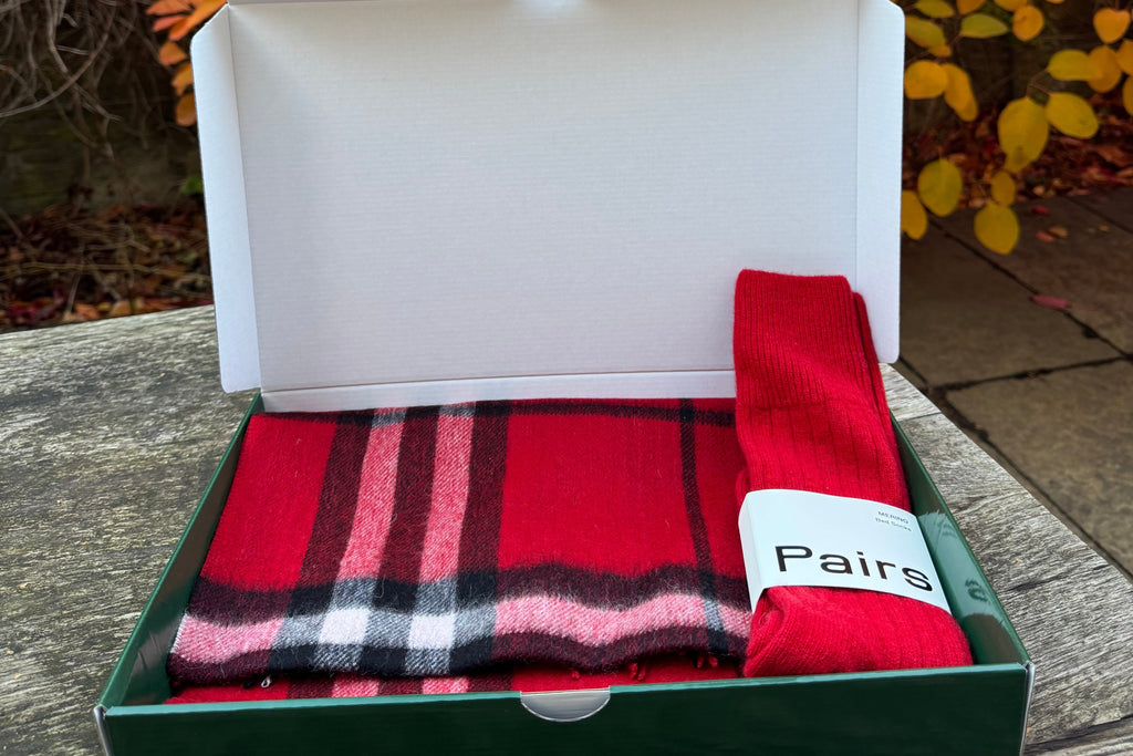 Red and black plaid scarf in a box with a blurred autumn leaf background