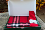 Red and black plaid scarf in a box with a blurred autumn leaf background