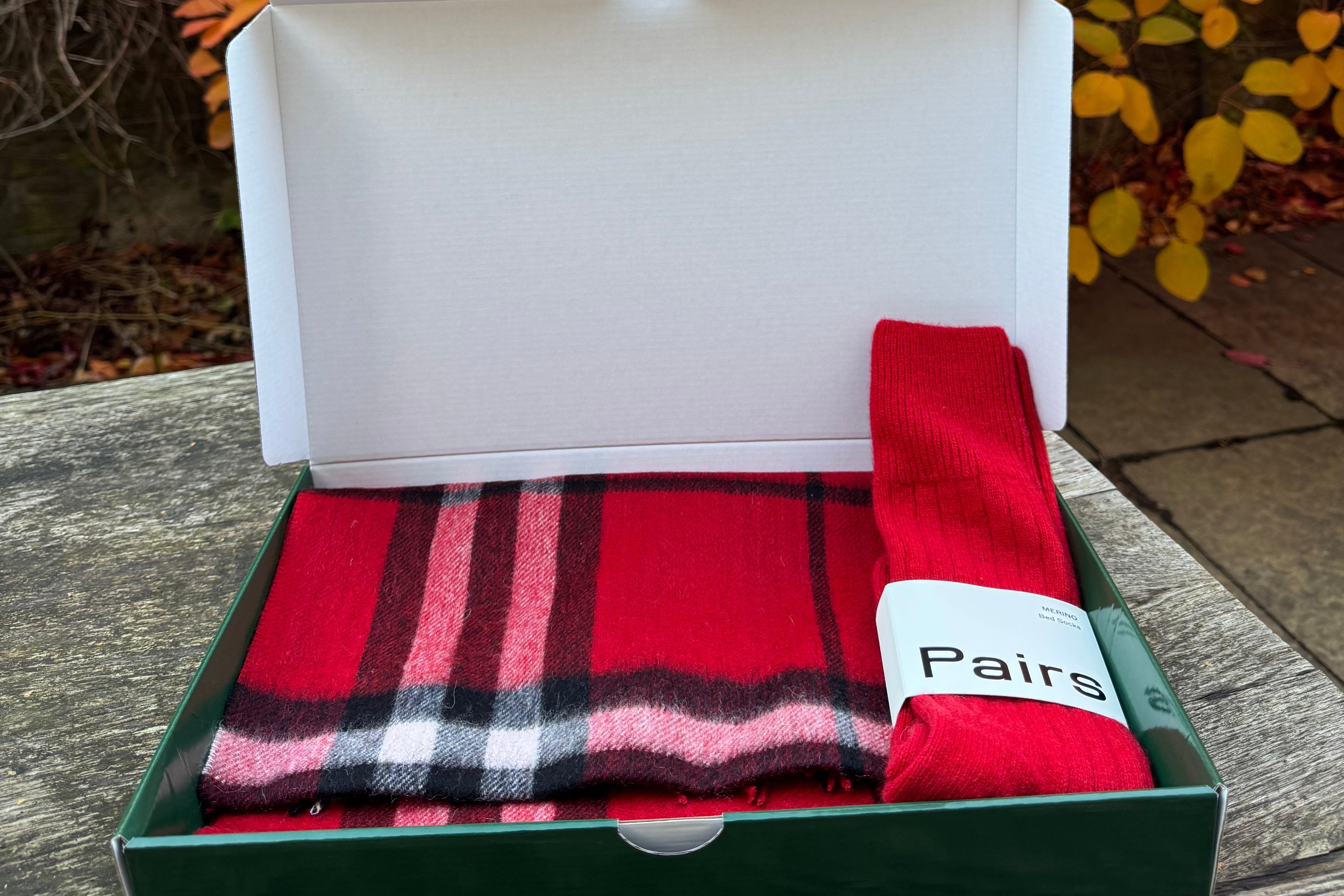 Red and black plaid scarf in a box with a blurred autumn leaf background